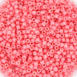 May include: A close-up view of a large quantity of small, round, pink beads. The beads are all the same size and shape, and they are arranged in a random pattern.