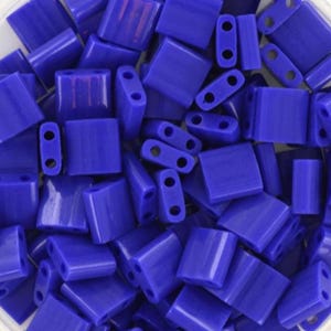Könnte beinhalten: Nahaufnahme von zahlreichen rechteckigen, tiefblauen Perlen, jede mit zwei Löchern. Die Perlen haben eine einheitliche Farbe und eine glatte, glänzende Oberfläche. Geeignet für die Schmuckherstellung und verschiedene Bastelprojekte.