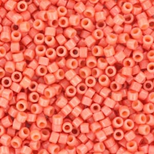 Puede incluir: Una imagen de primer plano de una gran cantidad de pequeñas cuentas redondas de color coral. Las cuentas son de plástico y tienen un acabado liso y brillante.