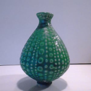 May include: A green ceramic vase with a textured surface of raised dots. The vase has a bulbous body and a narrow neck. The color transitions from a deep teal at the base to a lighter green at the top. The vase is approximately 6 inches tall.
