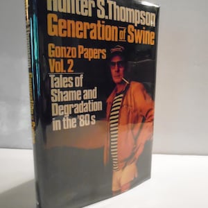 May include: A hardback book titled Generation of Swine by Hunter S. Thompson, featuring a black dust jacket with yellow and white text. The cover displays a photograph of a person wearing a striped shirt, jacket, and cap, holding a cigarette.