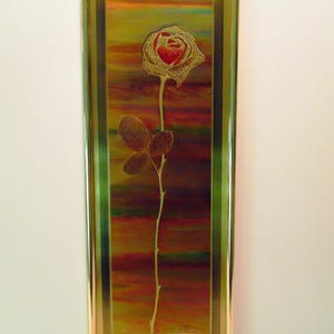 May include: A vertical rectangular wall art piece featuring a single rose with a red centre and gold-toned petals, stem, and leaves. The rose is set against a multi-coloured, iridescent background of orange, yellow, and green, enclosed in a gold frame.