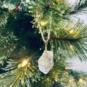 May include: A clear crystal ornament wrapped in gold wire, hanging from a gold string on a green Christmas tree.