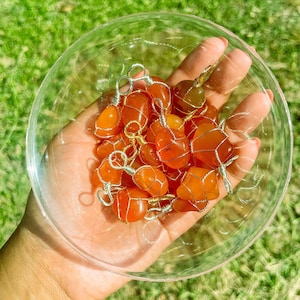 May include: A collection of carnelian stones wrapped in gold wire. The stones are a vibrant orange color and are displayed in a clear glass bowl.