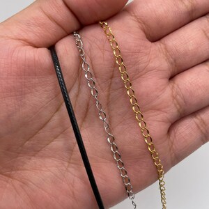 K&ouml;nnte beinhalten: Drei verschiedene Kettenarten f&uuml;r Halsketten: eine schwarze Schnur, eine silberne Kette und eine goldene Kette.
