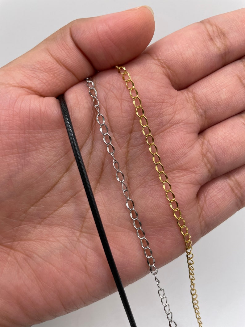 K&ouml;nnte beinhalten: Drei verschiedene Kettenarten f&uuml;r Halsketten: eine schwarze Schnur, eine silberne Kette und eine goldene Kette.