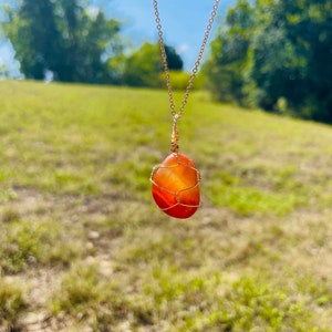 May include: A carnelian gemstone pendant necklace with a gold chain. The carnelian is wrapped in gold wire and has a natural, irregular shape.