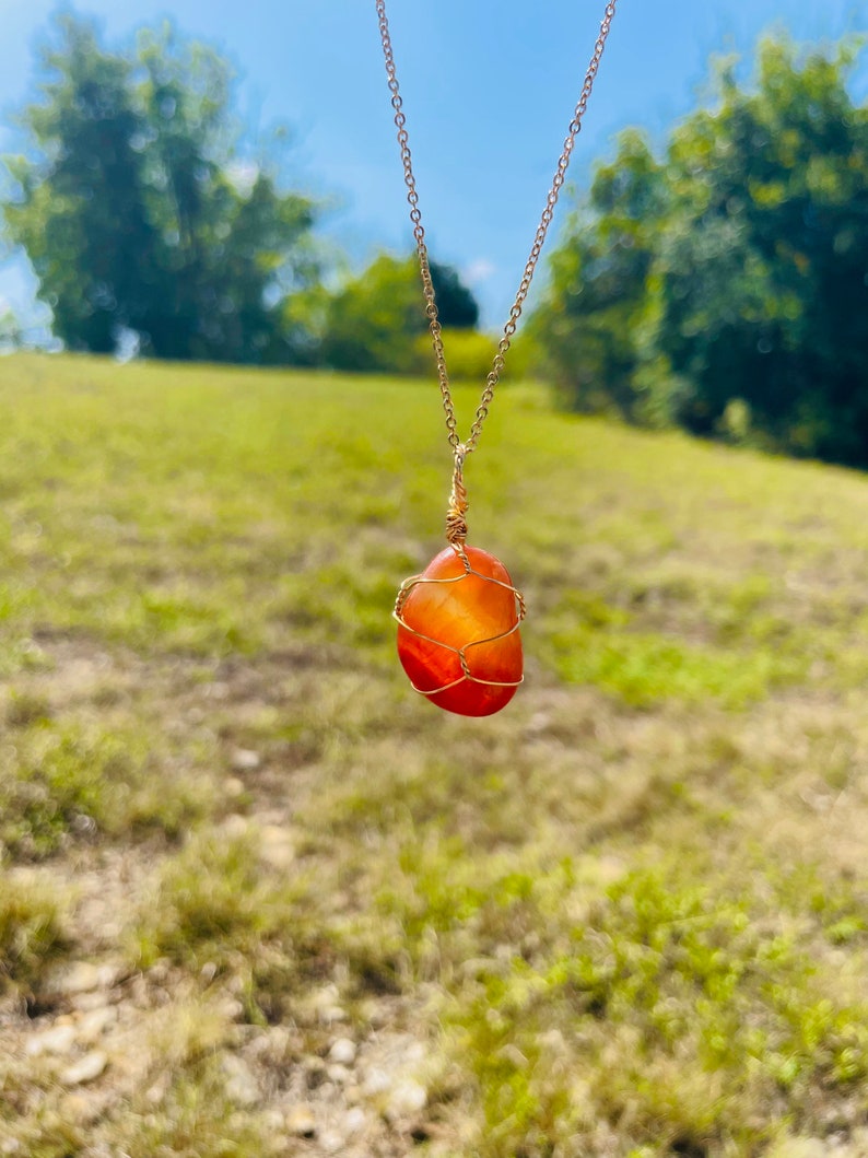 May include: A carnelian gemstone pendant necklace with a gold chain. The carnelian is wrapped in gold wire and has a natural, irregular shape.