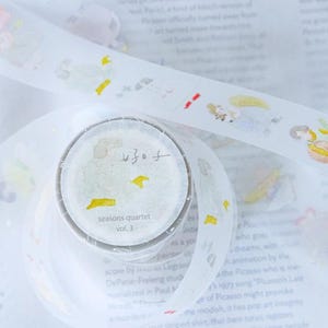 Może przedstawiać: Rolka ozdobnej taśmy washi o fantazyjnym wzorze. Taśma zawiera ilustracje postaci i żółtych kształtów na białym tle. Rolka taśmy zawiera tekst "seasons quartet vol. 3" oraz japońskie znaki.