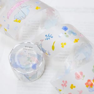 以下が含まれることがあります： 水彩デザインの装飾和紙テープのロール。テープには、傘を持った人、花、そして「pitter-patter」のテキストのイラストが描かれています。テープは白で、ピンク、青、黄色などのパステルカラーです。