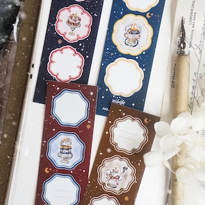 May include: Four rectangular sticker sheets featuring scalloped-edge frames, illustrations of cakes and teapots, and starry night motifs. The sheets are colored in dark blue, navy, maroon, and brown, with text reading Midnight Patisserie.