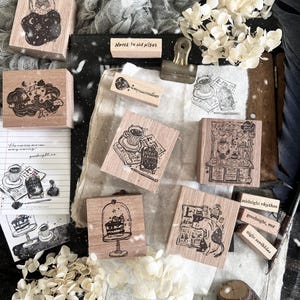 May include: A collection of square and rectangular wooden rubber stamps featuring black ink illustrations of night-themed scenes, including a sleeping figure, a cake under a glass dome, a cat, and coffee, with text labels like Notes in the night.