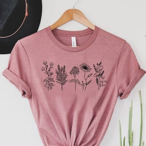 May include: A dusty rose t-shirt with a black line drawing of a row of flowers on the front.