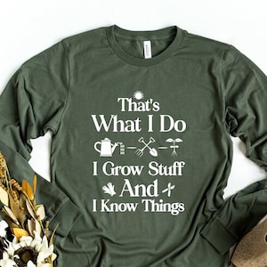 May include: A green long-sleeved t-shirt with a white graphic that says "That's What I Do I Grow Stuff And I Know Things". The graphic includes a watering can, a shovel, a rake, and a plant.