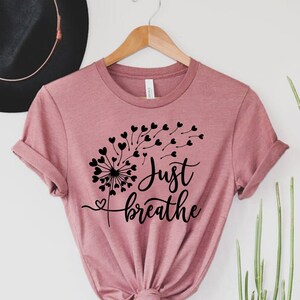 May include: A dusty rose colored t-shirt with a black dandelion graphic and the text "Just breathe".