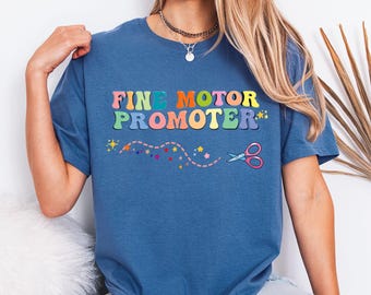 Może przedstawiać: Indygowa koszulka z napisem FINE MOTOR PROMOTER wykonanym wielokolorowymi, zaokrąglonymi literami. Pod napisem znajduje się grafika przerywanej linii z małymi kolorowymi gwiazdkami oraz nożyczkami z różowymi uchwytami na końcu linii.