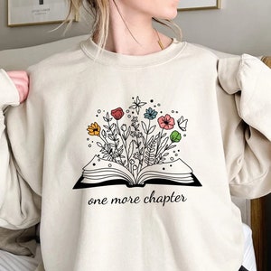May include: A beige sweatshirt with a graphic of an open book with flowers growing out of it. The text "one more chapter" is printed below the book.