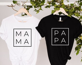 Puede incluir: Dos camisetas, una blanca y otra negra, con las palabras "MAMA" y "PAPA" impresas en un cuadrado en la parte delantera.