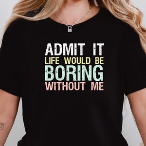 May include: Black t-shirt with the text "ADMIT IT LIFE WOULD BE BORING WITHOUT ME" in white, green, and pink. The shirt has short sleeves and a crew neck.