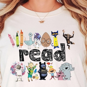 May include: A white t-shirt with a graphic of colorful characters and the word "read" in black. The characters include a bird, a cat, a monkey, a crayon, and an elephant. The shirt is labeled "Natural".