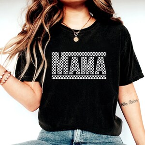 Puede incluir: Camiseta negra con la palabra "MAMA" en un patr&oacute;n de cuadros blancos y negros. La camiseta es de estilo casual, adecuada para el uso diario. El dise&ntilde;o est&aacute; centrado en la parte delantera.