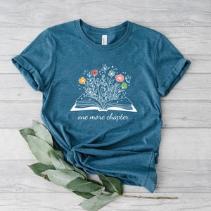 May include: Teal blue t-shirt with a white graphic of an open book with flowers growing out of it. The text "one more chapter" is printed below the book.