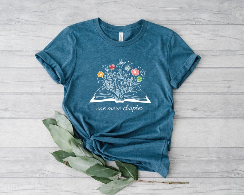 May include: Teal blue t-shirt with a white graphic of an open book with flowers growing out of it. The text "one more chapter" is printed below the book.