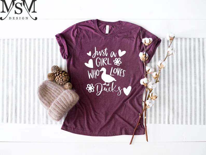 May include: A maroon t-shirt with the text "Just a girl who loves ducks" in white with a duck illustration and hearts.