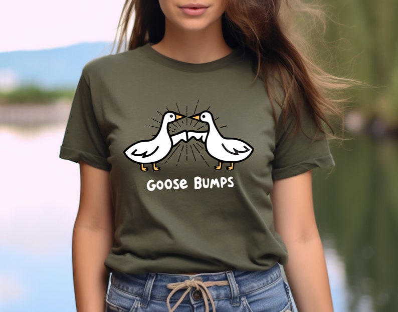 Puede incluir: Una camiseta verde con una ilustraci&oacute;n de dibujos animados de dos gansos blancos que se miran con el texto "Goose Bumps" debajo.