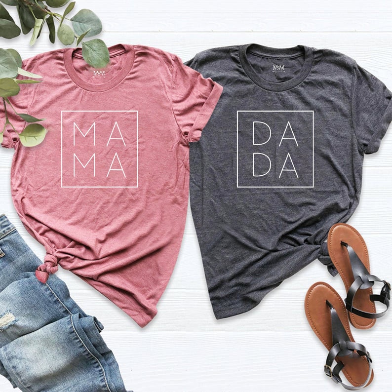 May include: Two t-shirts, one pink and one gray, with the words "MAMA" and "DADA" in white lettering inside a square on the front of each shirt.