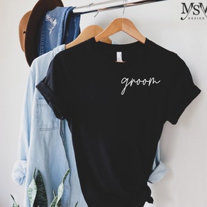 May include: Black t-shirt with the word "groom" written in white cursive script.