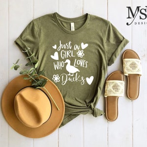 May include: Green t-shirt with white text that reads "Just a girl who loves ducks" with a duck silhouette and hearts.