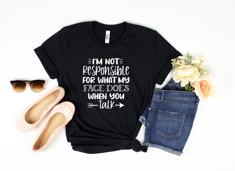 以下が含まれることがあります： I'M NOT RESPONSIBLE FOR WHAT MY FACE DOES WHEN YOU TALKという白い文字がプリントされた黒い半袖Tシャツ。ピンクのバレエシューズ、ダークブルーのデニムショートパンツ、茶色のサングラス、そして桃色の花の小さなブーケが添えられています。