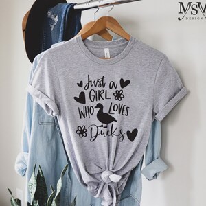 May include: A gray t-shirt with the text "Just a girl who loves ducks" in black lettering. The text is surrounded by hearts and flowers.