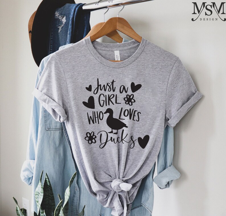 May include: A gray t-shirt with the text "Just a girl who loves ducks" in black lettering. The text is surrounded by hearts and flowers.