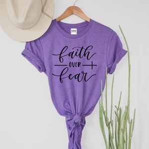 May include: Purple t-shirt with the text "faith over fear" in black script lettering.