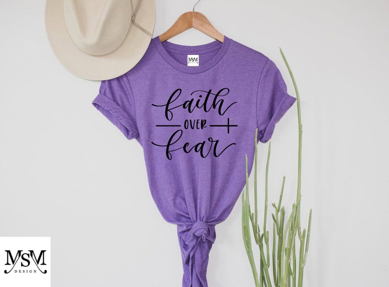 May include: Purple t-shirt with the text "faith over fear" in black script lettering.