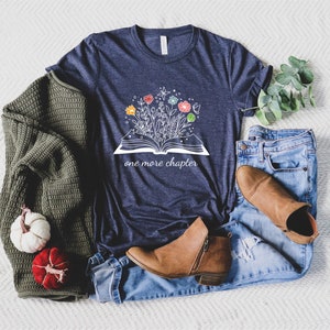 May include: A navy blue t-shirt with a white graphic of an open book with flowers growing out of it. The text "one more chapter" is printed below the book.