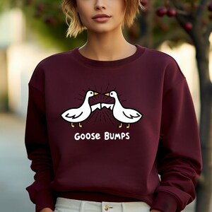 Puede incluir: Una sudadera color burdeos con un gr&aacute;fico blanco de dos gansos enfrentados con el texto "Goose Bumps" debajo.