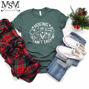 May include: Green t-shirt with white text that says "HOEING AIN'T EASY" and a graphic of gardening tools and plants.