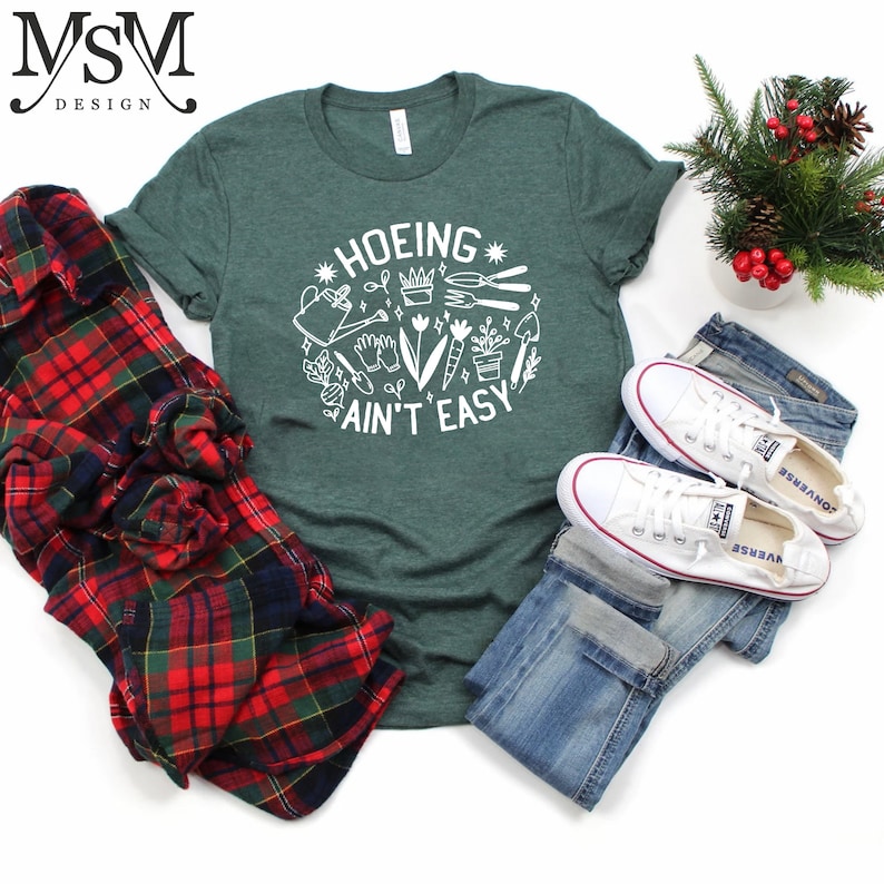 May include: Green t-shirt with white text that says "HOEING AIN'T EASY" and a graphic of gardening tools and plants.
