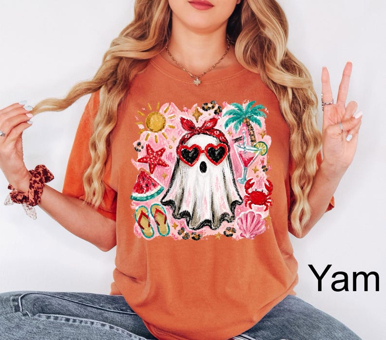 Puede incluir: Una camiseta de color naranja quemado con un gr&aacute;fico central de un fantasma blanco con una diadema roja y gafas de sol en forma de coraz&oacute;n. El dise&ntilde;o incluye elementos veraniegos como una palmera, una estrella de mar y un cangrejo.