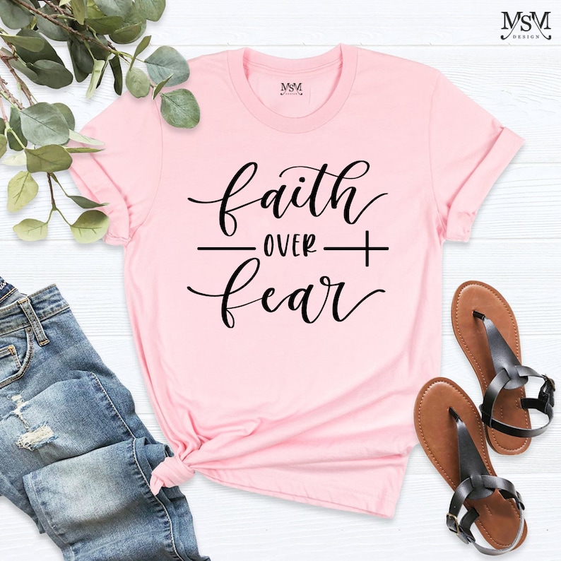 May include: Pink t-shirt with the text "faith over fear" in black cursive lettering.