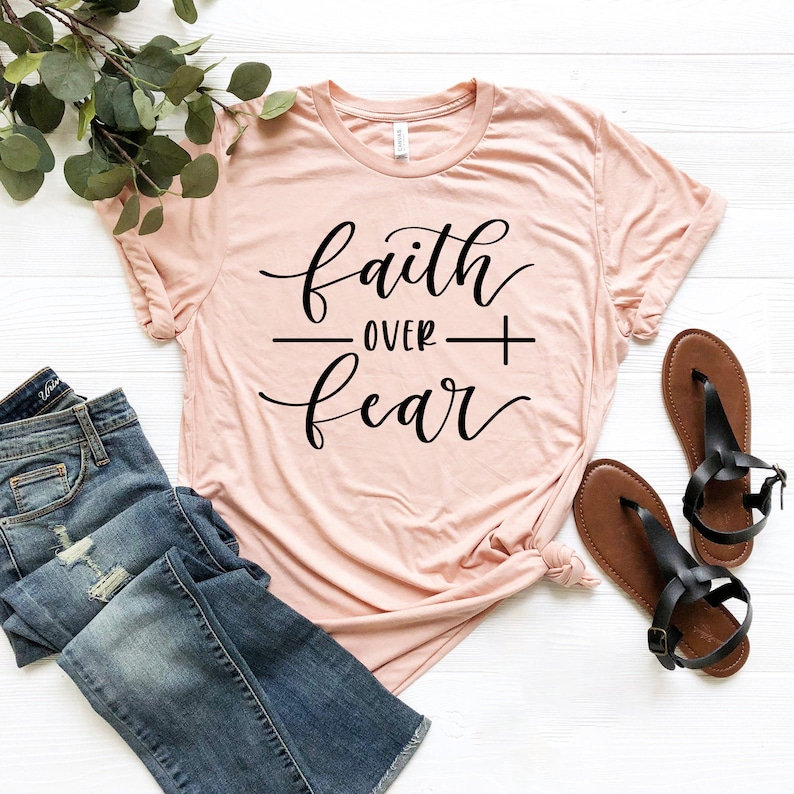 May include: A light pink t-shirt with the text "faith over fear" in black cursive lettering.