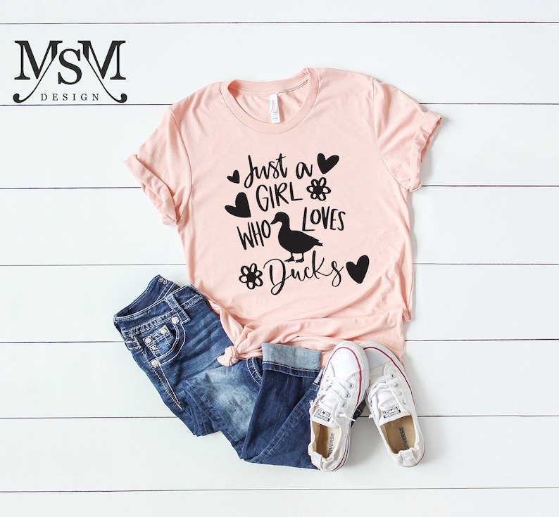 May include: A pink t-shirt with the text "Just a girl who loves ducks" in black lettering. The shirt features a black silhouette of a duck and hearts and flowers.