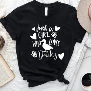 May include: Black t-shirt with white text that reads "Just a girl who loves ducks" with a white duck illustration and hearts and flowers.