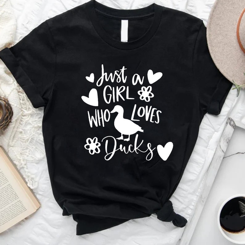 May include: Black t-shirt with white text that reads "Just a girl who loves ducks" with a white duck illustration and hearts and flowers.