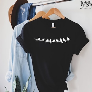 May include: Black t-shirt with a white silhouette of a line of birds on a wire.