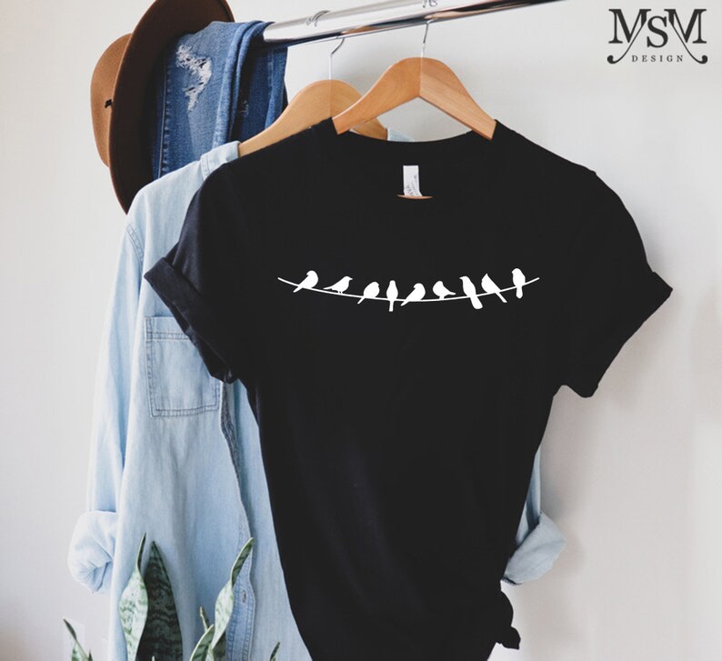 May include: Black t-shirt with a white silhouette of a line of birds on a wire.