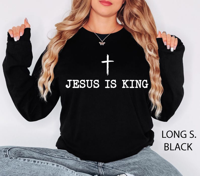 K&ouml;nnte beinhalten: Schwarzes Langarm-Sweatshirt mit dem wei&szlig;en Text &bdquo;JESUS IS KING&ldquo; und einem wei&szlig;en Kreuz. Das Kleidungsst&uuml;ck hat eine einfarbige schwarze Farbe.